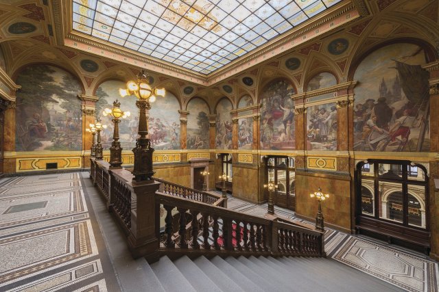Monumentální schodišťová hala, obložená žulou a mramorem, má šest nástěnných lunet od Karla Vítězslava Maška, další obrazy jsou od Karla Ladislava Klusáčka