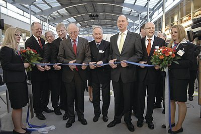 Slavnostní otevírací přestřižení pásky před zahájením veletrhu BAU 2009. Trojice uprostřed je (zleva)Günter Verheugen, viceprezident Evropské komise, Manfred Wutzlhofer, prezident společnosti Messe München GmbH a Wolfgang Tiefensee, německý ministr dopravy, stavebnictví a urbanismu.
