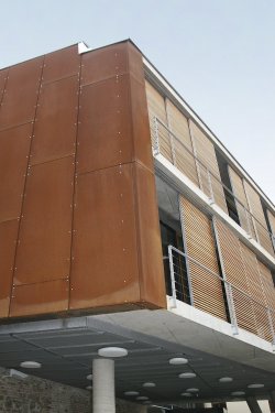 Detailní záběr na část nové budovy, kde je vidět spojení materiálů jako jsou lícové cihly, pohledový beton, ocel, dřevo a sklo