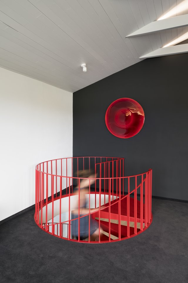 Abstraktní umělecké dílo zavěšené nad schodištěm pochází z dílny Milana Housera. Doplňuje schodiště a koberec ve stejné barvě.