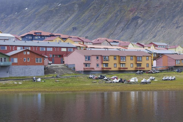 Barevné domy a zelená pole s arktickými květinami, vše na pozadí dramatické oblohy a pusté hory v Longyearbyenu, souostroví Špicberky, Norsko, 78. rovnoběžka s. š. Světlé barvy krom toho, že vytvářejí pozitivní atmosféru, zde plní stejnou funkci, jako v ostatních ilustracích tohoto článku. Foto: Shutterstock