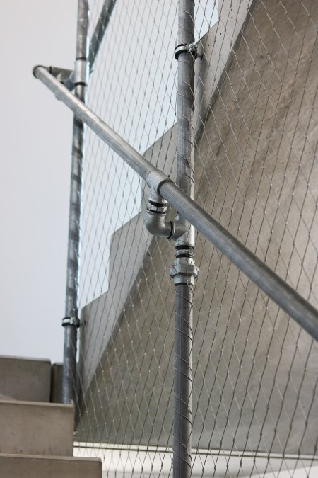 Zábradlí schodiště je tvořeno nerezovou sítí napnutou mezi vodovodními trubkami