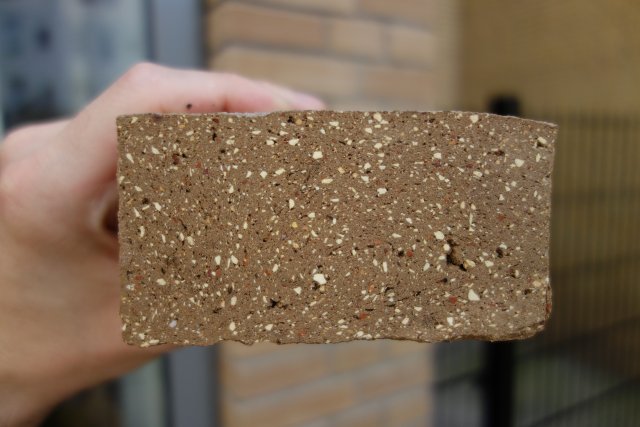 Řez cihlou, jejímž obsahem je recyklovaný materiál od keramiky přes sklo a izolační materiály až po hlínu.