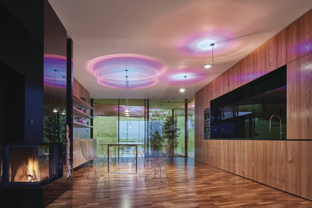 Iridescentní světlo rozptýlené čočkami s dvoubarevnými rozptylovými filtry pronikající skrze plochu stropu doplňuje přímé svícení nebarevným světlem.