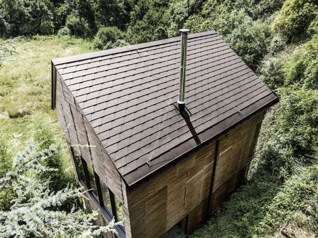  Sedlová střecha s asymetrickým sklonem je pokrytá PREFA falcovanými šindeli barvy P.10 oříšková. Barva střechy koresponduje s proutěnou vrbovou fasádou a okolím. Zdroj: PREFA Aluminiumprodukte / Croce & WIR