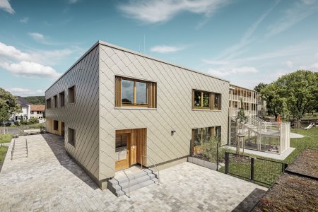  Hliníková fasáda technicky i vizuálně spojuje recyklovanou betonovou konstrukci a masivní dřevěnou konstrukci do
        jednoho celku.